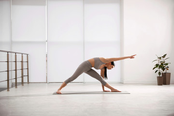 Young woman practicing triangle asana in yoga studio. Utthita Trikonasana pose