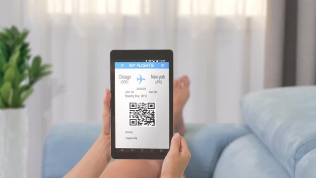 woman checks boarding pass flight ticket on tablet app at home