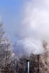 Beautiful winter day with white trees, blue sky and metal chimney with smoke