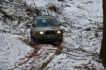 Obraz na płótnie Canvas Off-road car rides down hill on snow and mud in forest