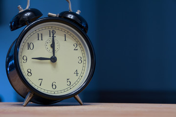 Vintage and retro analogue alarm clock indicating that it's nine o' clock, 9pm or 9am, on a dark...
