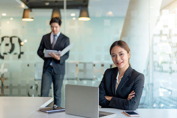 Portrait of young asian businesswoman sitting at her office looking at camera. background of businessman.