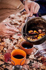 In nature, in the forest, they cooked real hot mulled wine at the stake in the autumn. Pours compote into a cup for himself and his girlfriend to keep warm.