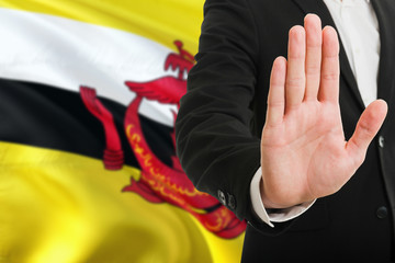 Brunei rejection concept. Elegant businessman is showing stop sign with hand on national flag background.