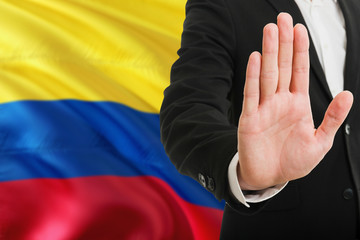 Colombia rejection concept. Elegant businessman is showing stop sign with hand on national flag background.