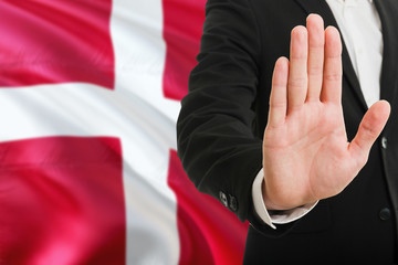 Denmark rejection concept. Elegant businessman is showing stop sign with hand on national flag background.