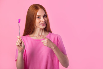 beautiful young woman with red hair on a pink background with a toothbrush