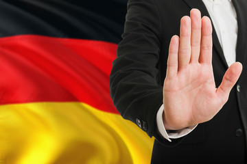 Germany rejection concept. Elegant businessman is showing stop sign with hand on national flag background.