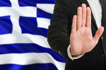 Greece rejection concept. Elegant businessman is showing stop sign with hand on national flag...