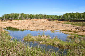 Development of sand quarry. Excavators and mining equipment in the distance. Flooded spent part of the quarry. Extraction of sand and building material.