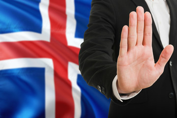 Iceland rejection concept. Elegant businessman is showing stop sign with hand on national flag background.