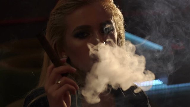 Close-up of a girl Smoking a cigar, she blows a lot of smoke on the camera. Slow motion. Close-up of a sexy woman Smoking a cigar in a bar in a cafe.