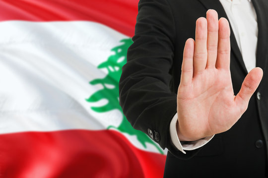 Lebanon rejection concept. Elegant businessman is showing stop sign with hand on national flag background.