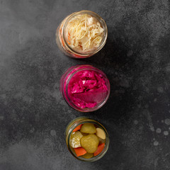 various fermented vegetables in jars (pickled cabbage, pickled cucumbers). dark background, top view, close-up