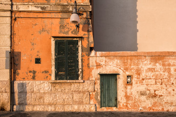 Stone wall of the building, morning sun, orange color. Closed window and door, Polignano, Italy.