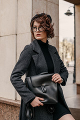 Outdoor fashion portrait of young elegant woman wearing total black outfit: classic coat,...