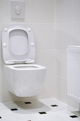Interior. A white toilet bowl hangs on a white tile wall in a white bathroom