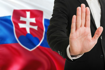 Slovakia rejection concept. Elegant businessman is showing stop sign with hand on national flag background.