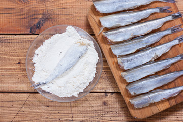 Step-by-step cooking of fried smelt in a pan, step 4 - breading in the meal of raw fish smelt, top view, selective focus