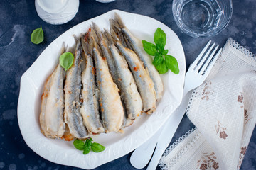 Whole grilled smelt fish on a white dish, selective focus, top view