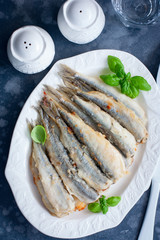Whole grilled smelt fish on a white dish, selective focus, top view