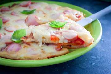 Pizza with tomatoes and sausages cooked in a pan, selective focus