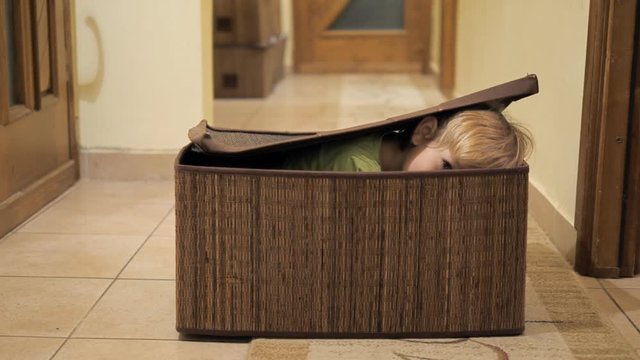 Little funny child playing home hide and seek, opens up the lid of box and spy
