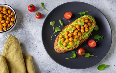 avocado toast with roasted chickpeas, herbs, cherry on a dark plate. vegan snack. gray background, horizontal image