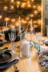 Wooden table setting with burning candles and Christmas decorations.holiday living room.magic New year.Festive living room decorated for Christmas and New Year with stylish table set. Shiny garland.