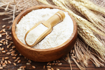 Wheat flour in wooden spoon on wheat ears plants background, rustic farmer card, selective focus	