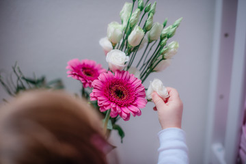 Kind von hinten erkundet einen Blumenstrauß mit pinken Gerbera und weißen Blumen vor hellem...