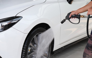 Closeup of white car cleaning, washing with high pressure water spraying by male worker. 