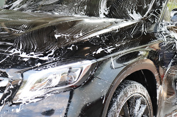 Closeup of black car cleaning, washing with  high pressure foam spraying at car care service center.