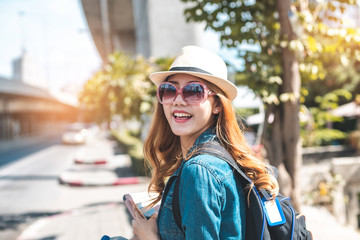 Happy Asian woman traveler holding a mobile phone in station and waiting for train in vacation time. Young Asian Tourists With Backpacks Train travel in Sightseeing City Thailand.