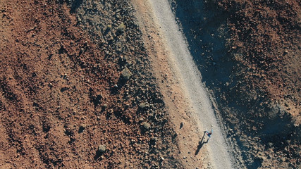 View from above. A woman runs along the path in the mountains, around the volcanic sand and frozen lava