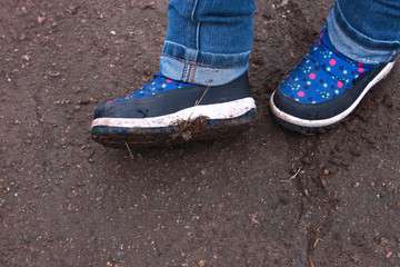 Kids boots in muddy puddle. Colorful winter outdoor rain shoes on childrens feet in action. A child on a walk stay in the mud. Choosing footwear for an active lifestyle. Autumn rainy weather.