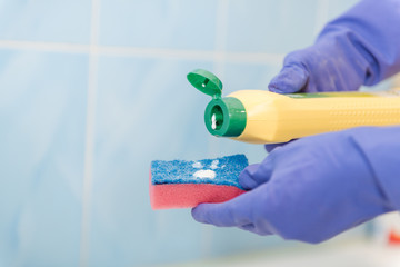 The girl cleans up in the bathroom, pour cleaning agent on the sponge, the girl cleans up in rubber gloves