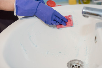 The girl cleans the bathroom, clean the ceramic sink in the bathroom, wash with rubber gloves,...