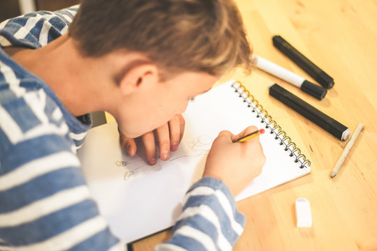 Close up view of student drawing with pencil. Boy doing homework writing on a paper. Kid hold a pencil and draw a manga at home. Teen drawing sitting at the table. Education art talent ability concept
