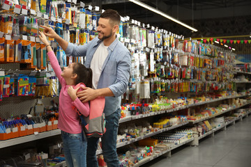 Little girl with father choosing school stationery in supermarket