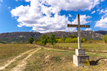 Fototapeta na wymiar Stone cross on the mountain above clouds against blue sky
