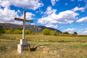 Fototapeta na wymiar Stone cross on the mountain above clouds against blue sky