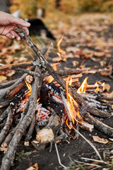 The guy throws a branch into the fire. Camping in the fall.
