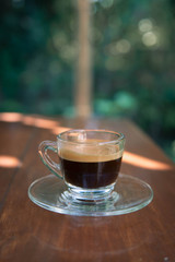cup of hot espresso on wood table with  green garden background. relaxing coffee concept
