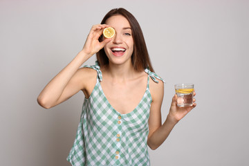 Young woman with glass of lemon water on light background