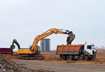 Excavator load the sand to the heavy dump truck on construction site. Excavators and dozers digs the ground for the foundation and construction of a new building. Apartment renovation program © MaxSafaniuk