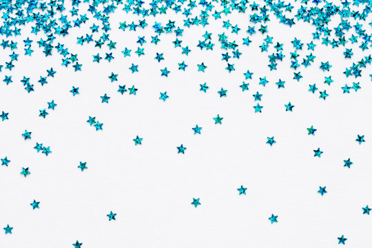 Iridescent Blue color falling stars. Glitter confetti on white festive background. Holiday Sparkling Frame. Flat lay.