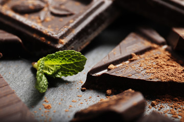 Broken dark chocolate pieces, mint and cocoa powder on dark background close-up