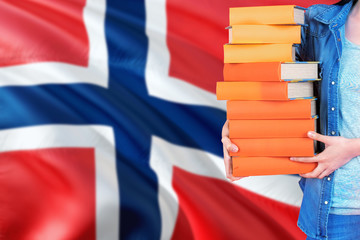 Norway national education concept. Close up of female student holding colorful books with country flag background.