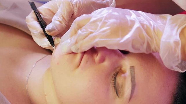 The beautician plucks hairs from the chin and above the client's upper lip with tweezers